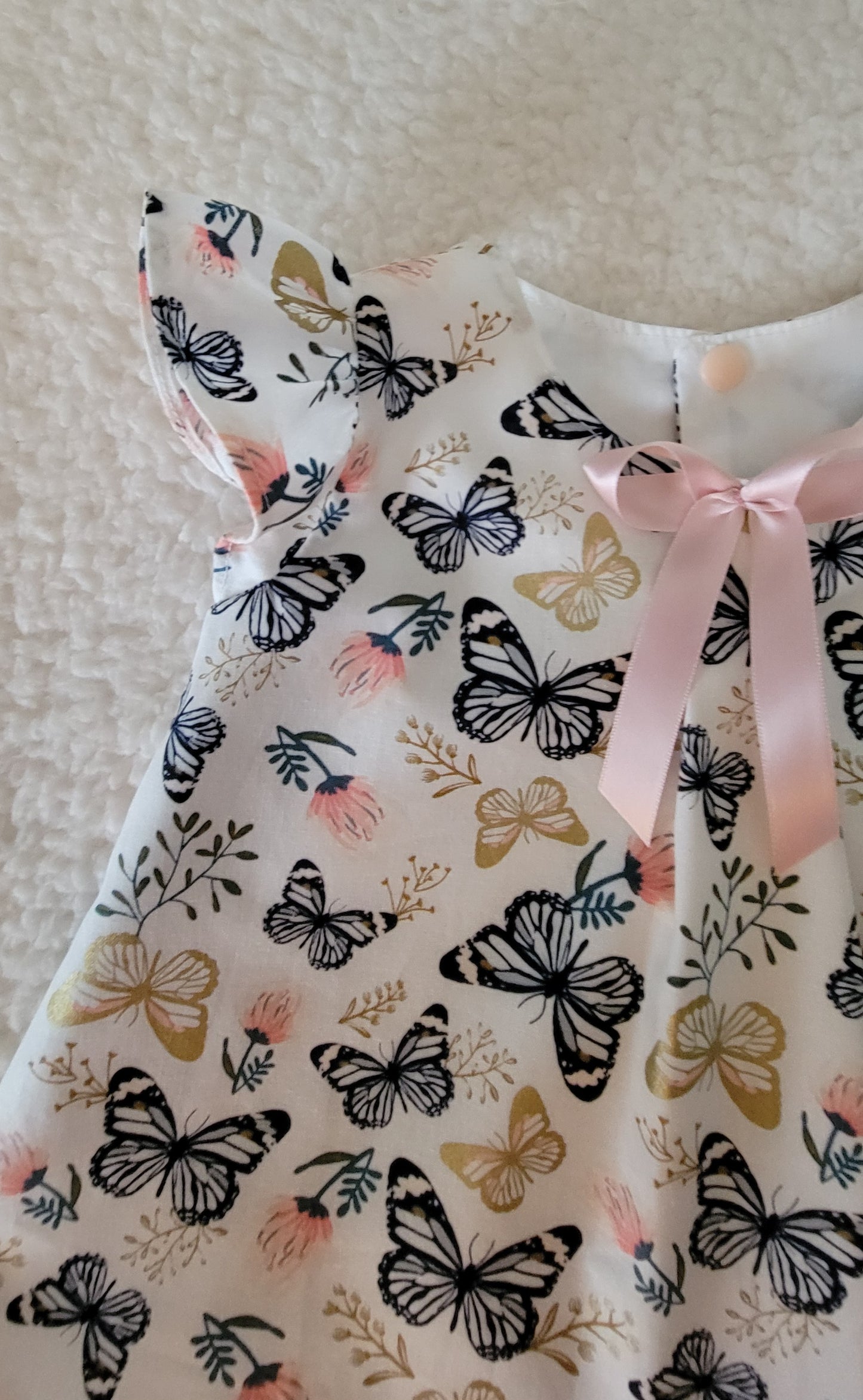 Dress with butterfly pattern and pink ribbon on a neutral background