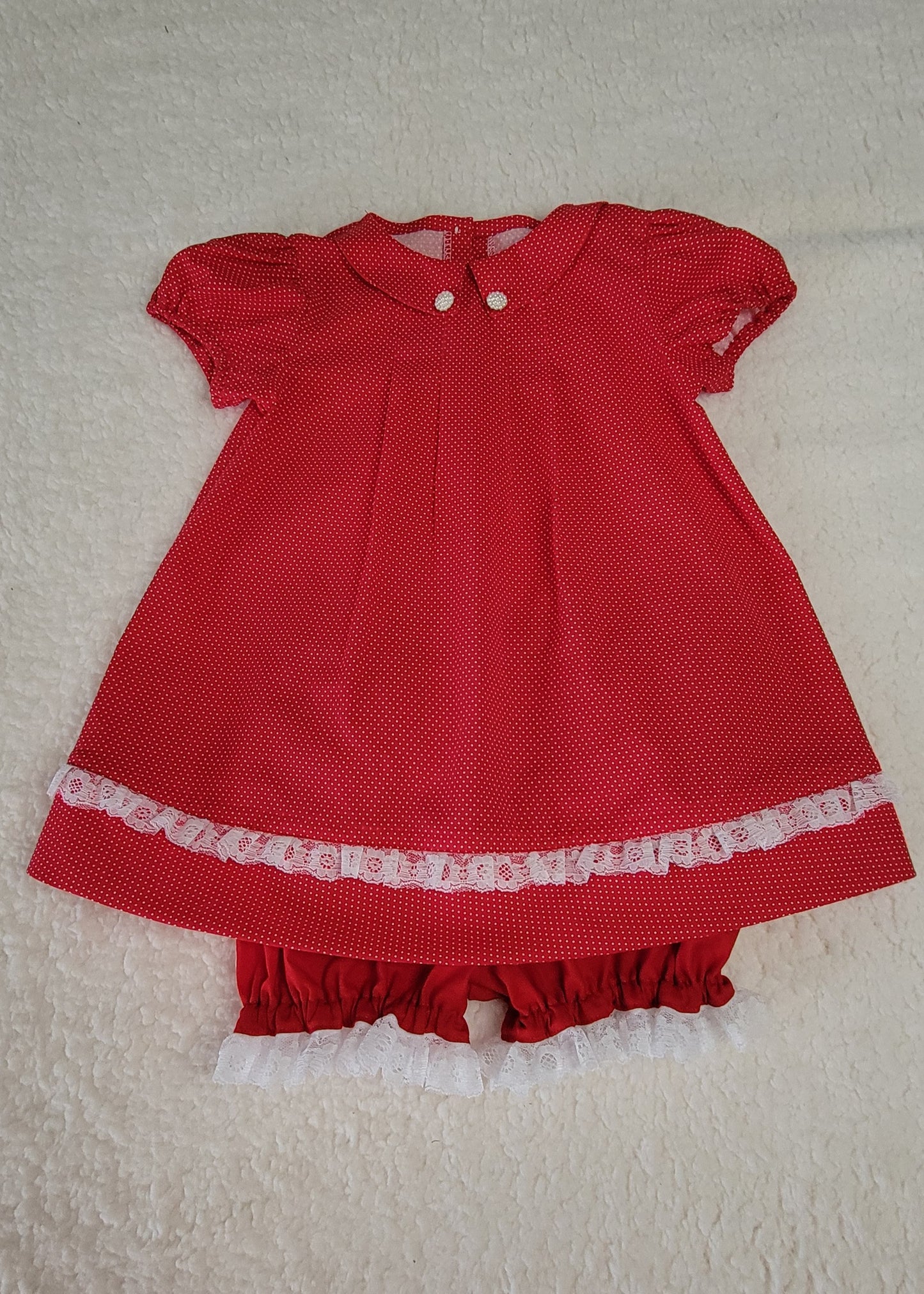 Red baby dress with white lace trim on a beige background