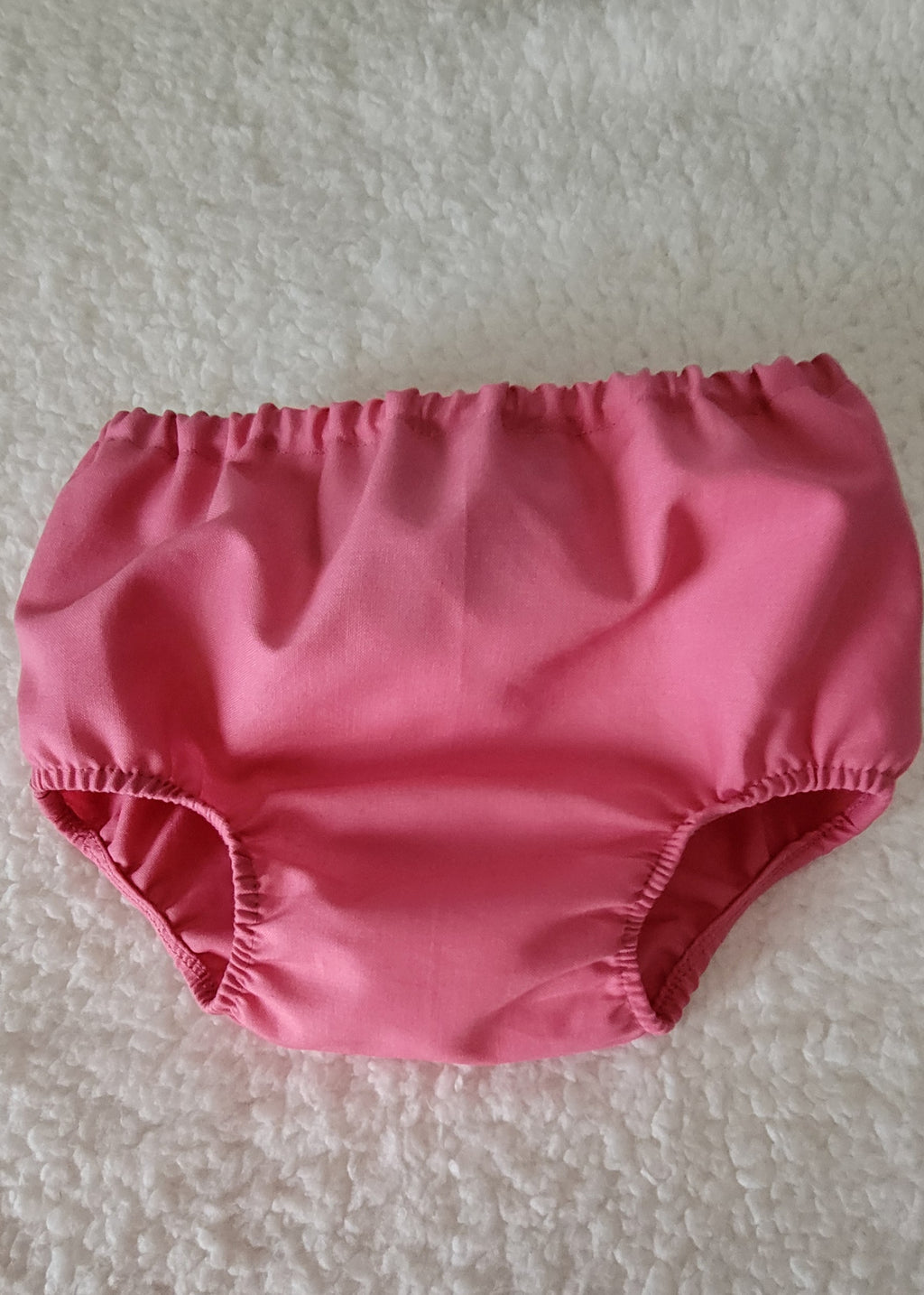 Pink baby bloomers on a textured white background