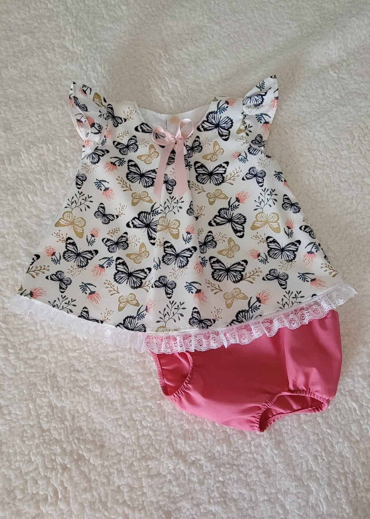 Baby outfit with butterfly-patterned top and pink bloomers on a textured surface