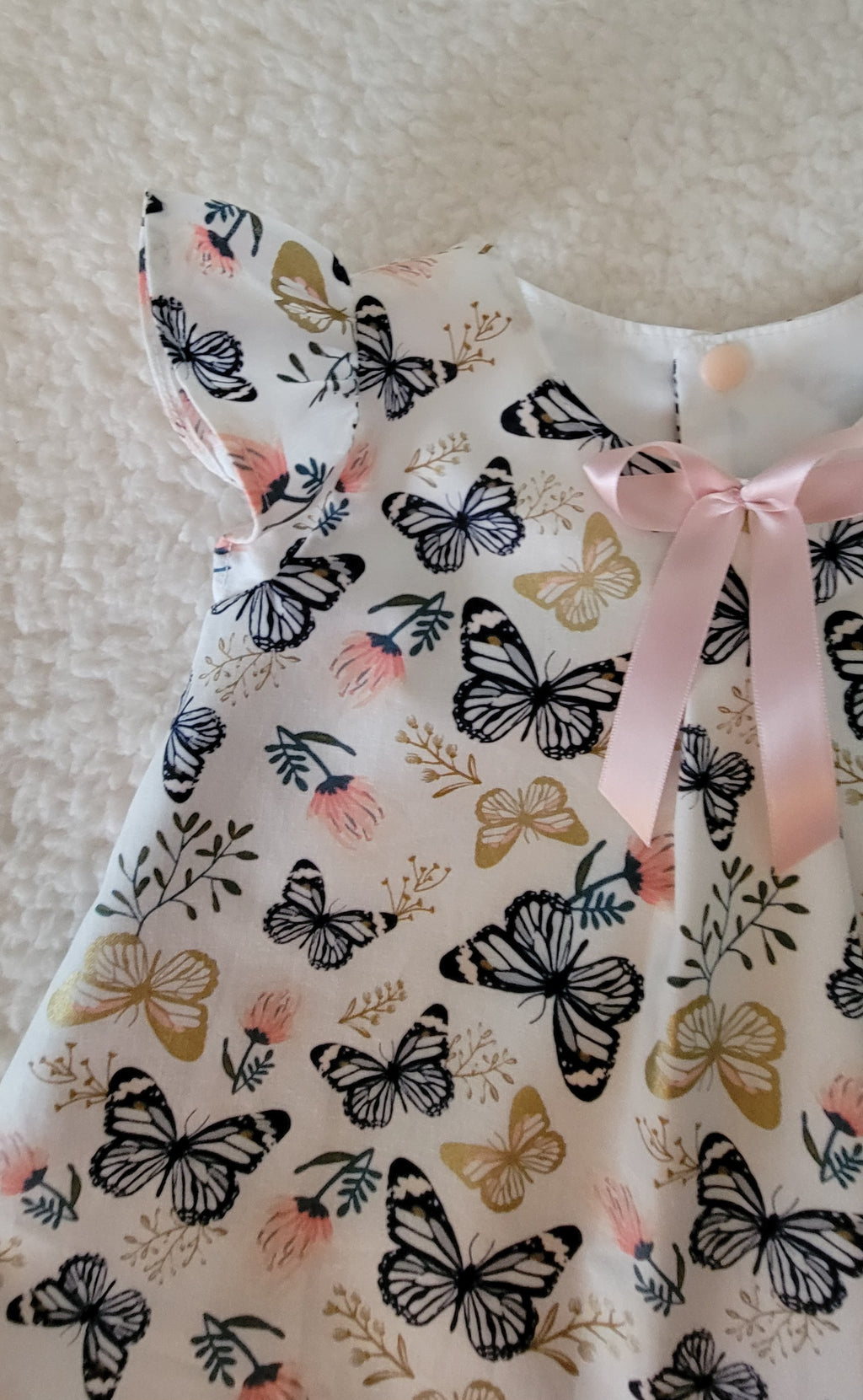 Dress with butterfly pattern and pink ribbon on a neutral background
