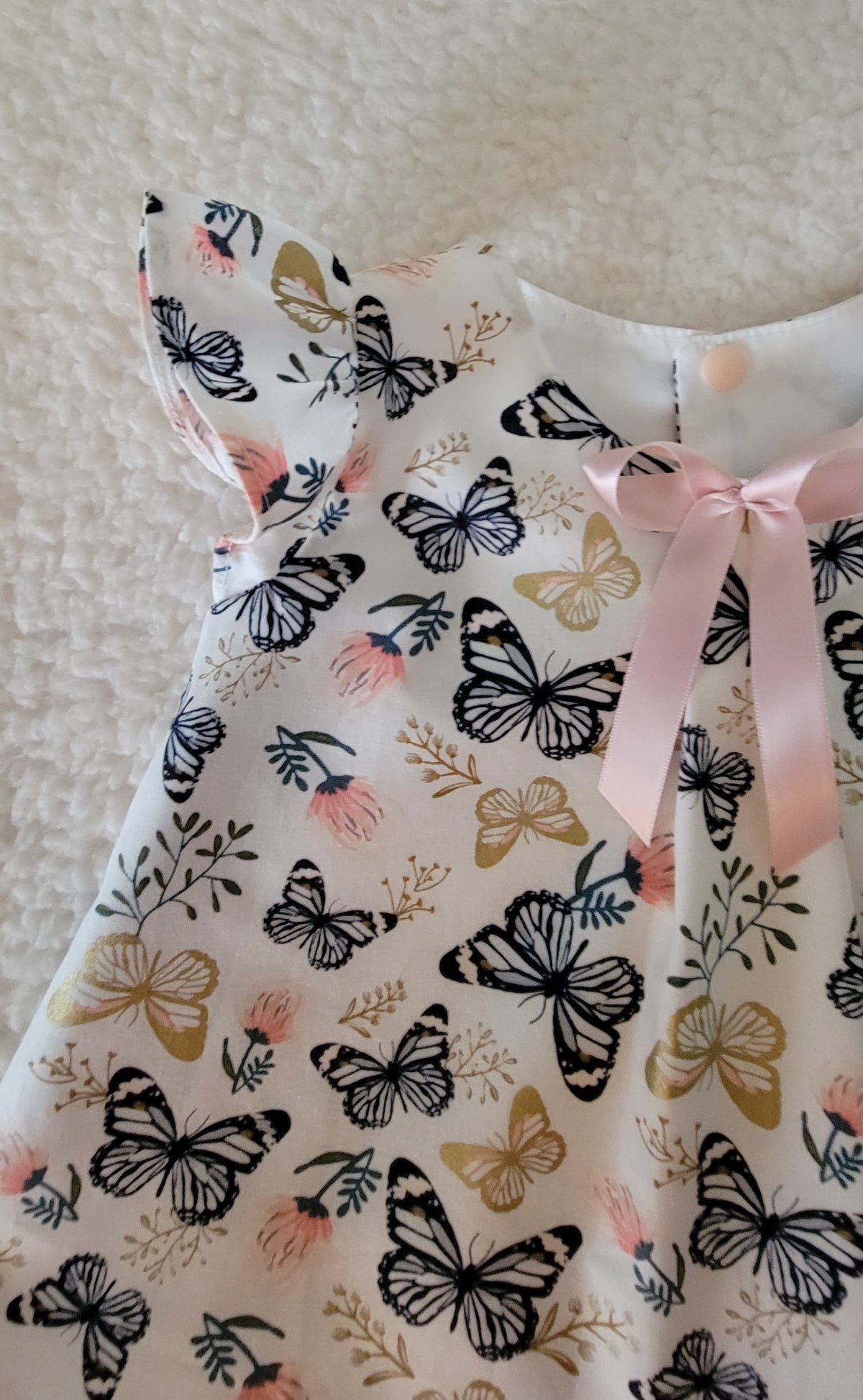 Dress with butterfly pattern and pink ribbon on a neutral background