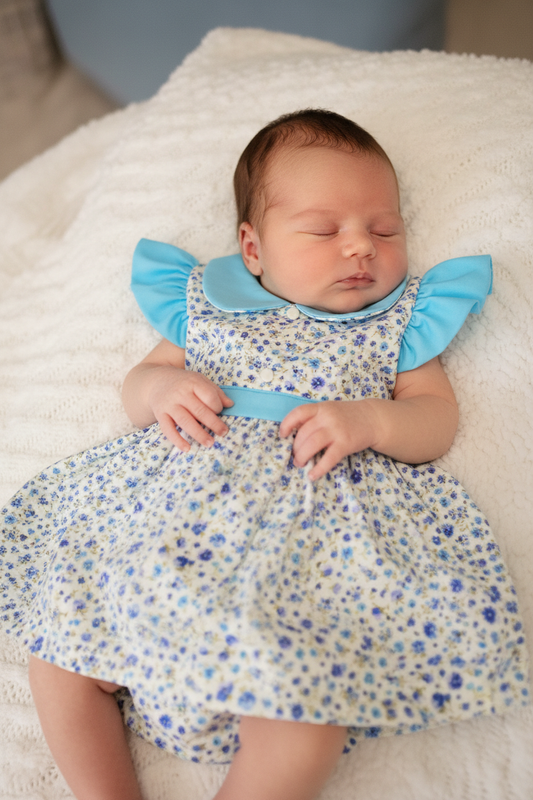 Newborn baby girl in light blue dress with collar and floral bloomers - gentle lighting