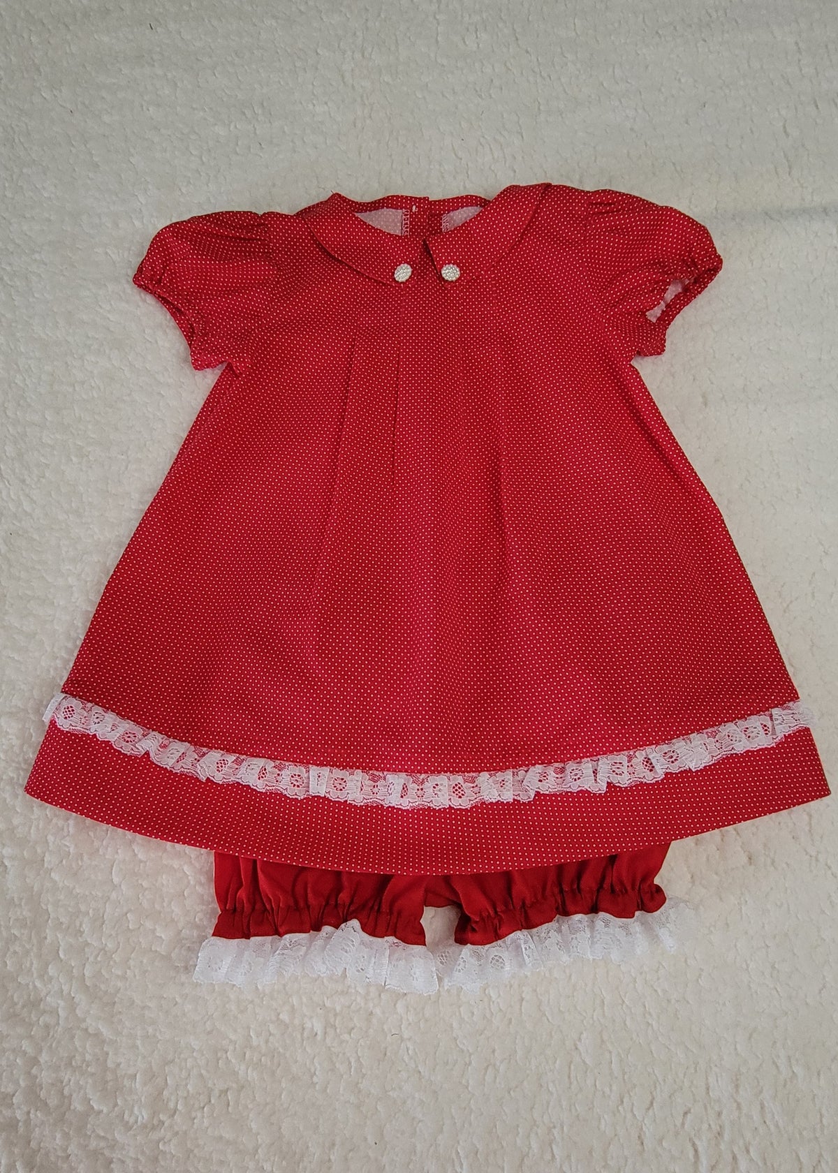 Red baby dress with white lace trim on a beige background